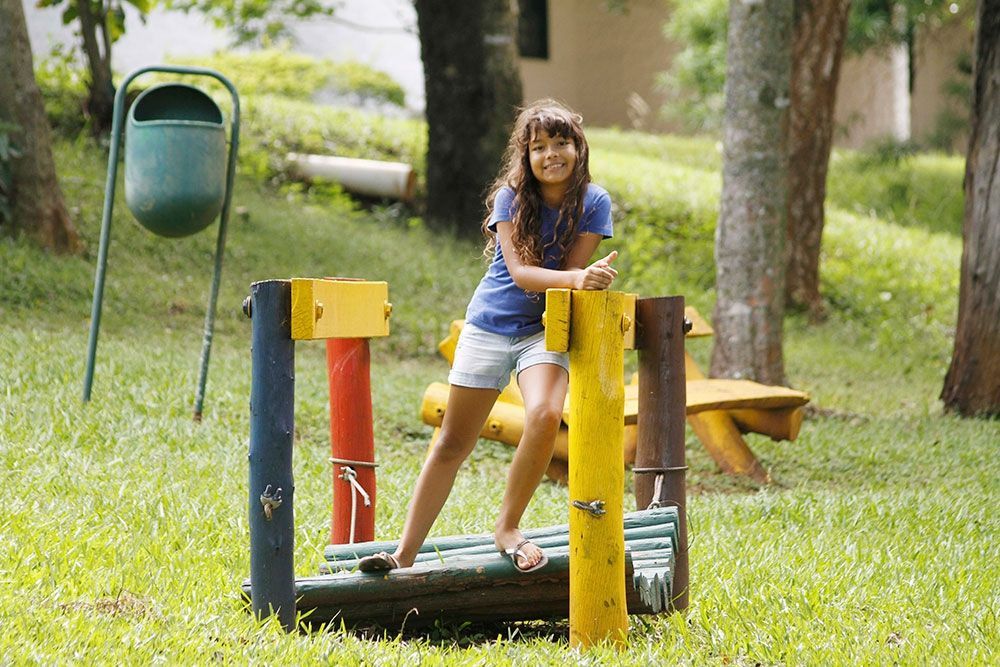Uma menina está sentada em uma estrutura de madeira em um parque.