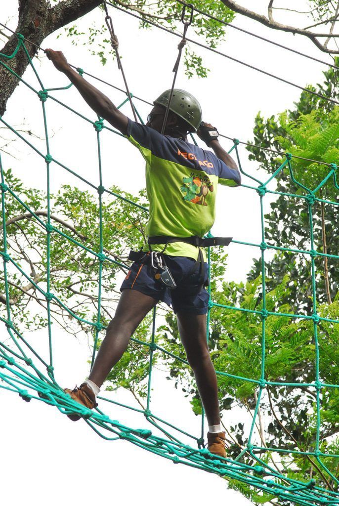 Um homem usando um capacete está caminhando sobre uma ponte de corda.