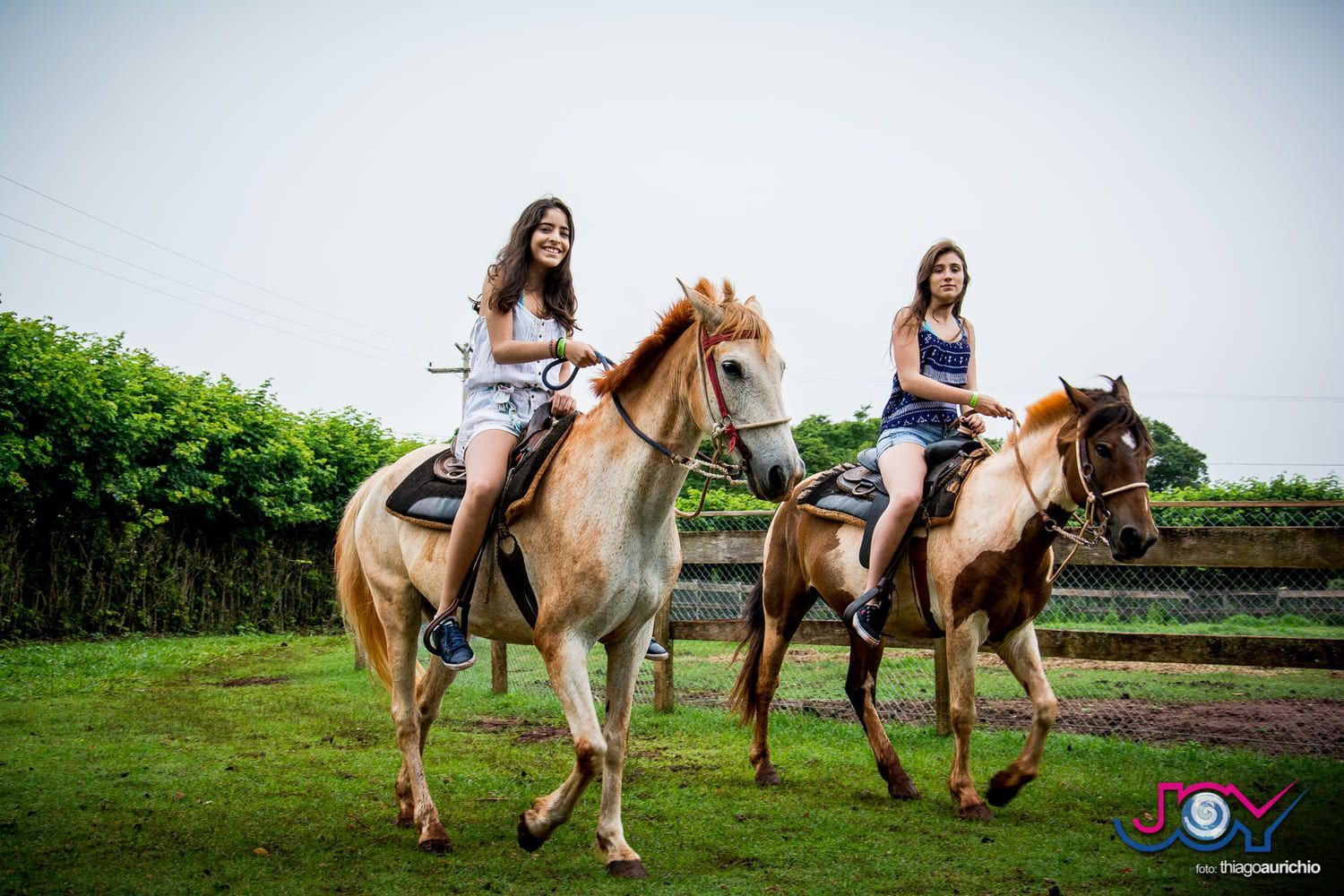 Duas jovens mulheres estão cavalgando em um campo.