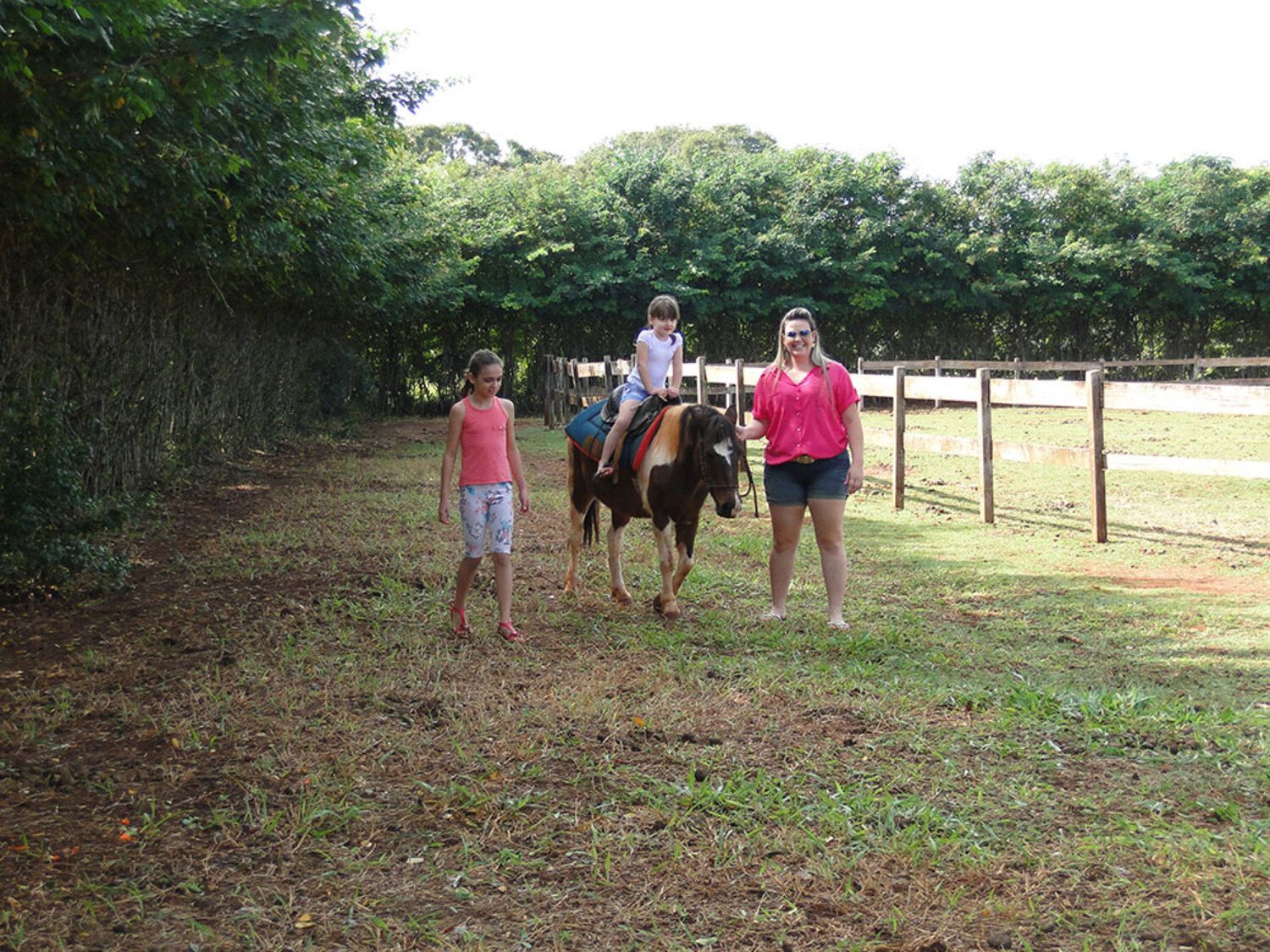 Uma menina está cavalgando em um campo com duas mulheres em pé atrás dela.