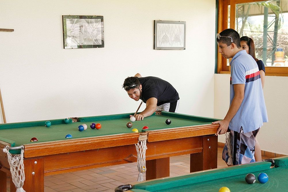 Dois homens estão jogando sinuca em uma sala com duas mesas de sinuca
