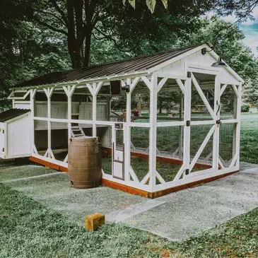 A large white chicken coop is sitting in the middle of a lush green field.