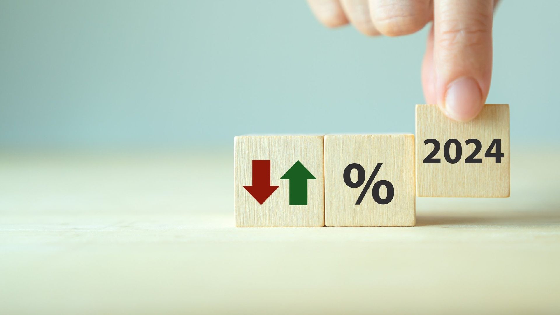 Hånd, der placerer 2024-blok ved siden af ​​blokke med op/ned-pile og et procentsymbol, hvilket antyder økonomisk prognose.