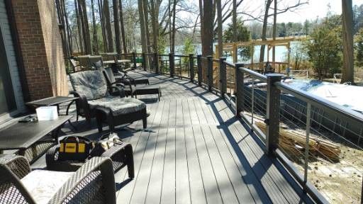A partially built wood deck attached to a gray house, featuring white railings and a view of trees in the background.