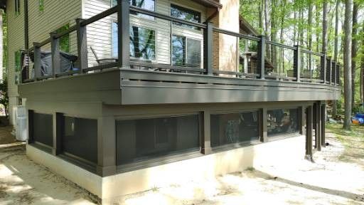 A sunlit wooden deck featuring an outdoor dining set next to a glass-walled structure overlooking a forested landscape.