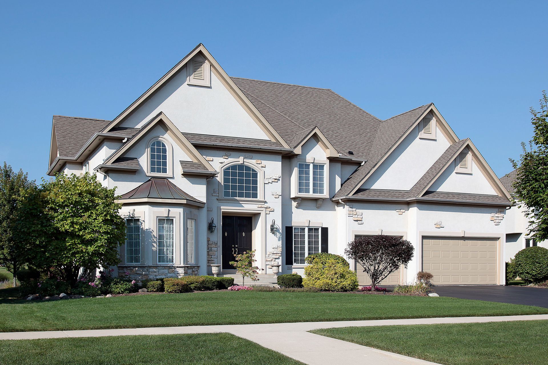 A large two-story white suburban house with a brown shingled roof, a front lawn, and an attached two-car garage.