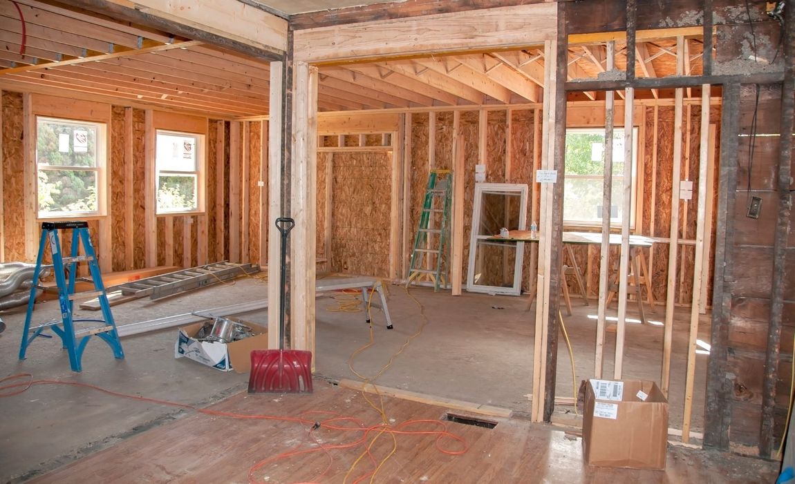 A house under construction with exposed wooden framing for porches, grey exterior panels, and a shingled roof.