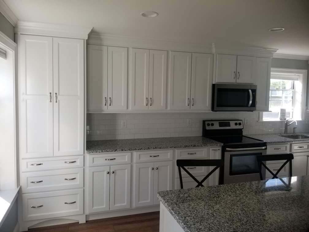 A bright kitchen with white cabinets, speckled granite countertops, a built-in pantry, and stainless steel appliances.