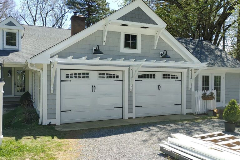 A covered balcony featuring a gray wicker sectional sofa with red pillows, a square fire pit, and a gray side table.