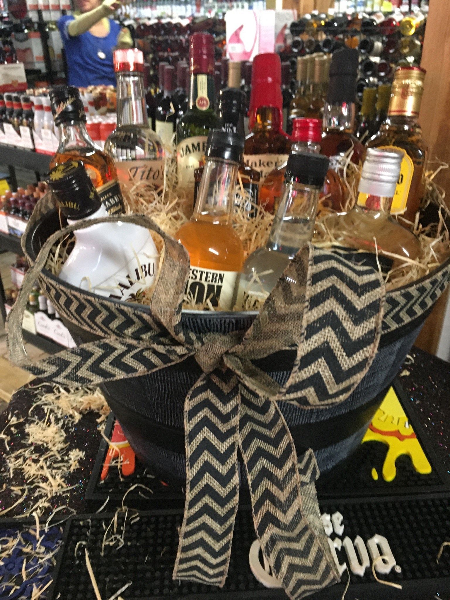 Gift basket overflowing with various liquor bottles, tied with a chevron patterned ribbon.