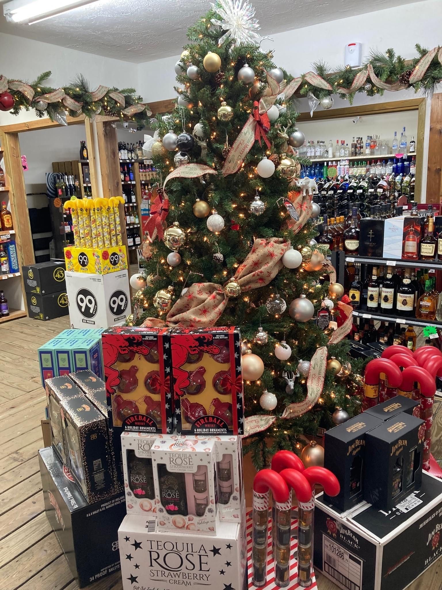 Christmas tree in a liquor store, surrounded by gift boxes and bottles, festive decorations.