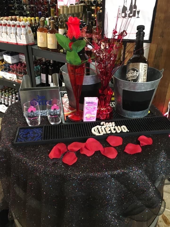A festive liquor display with roses, bottles, and glasses on a sparkly black table, likely for Valentine's Day.