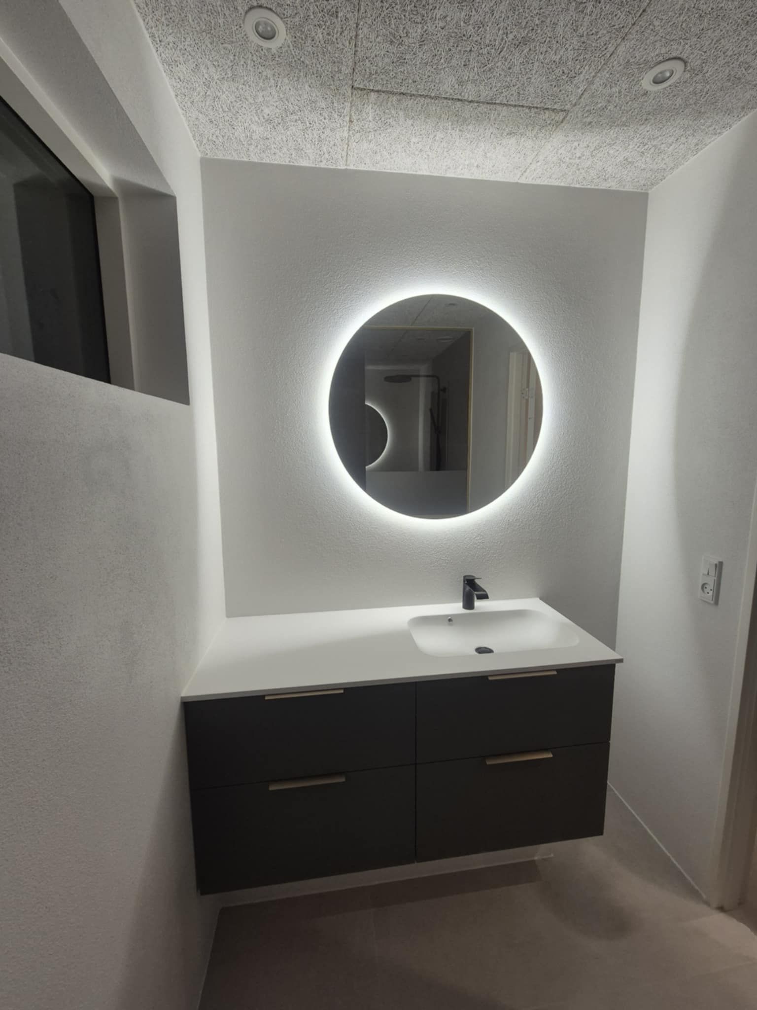 Et badeværelse med en vask og et rundt spejl