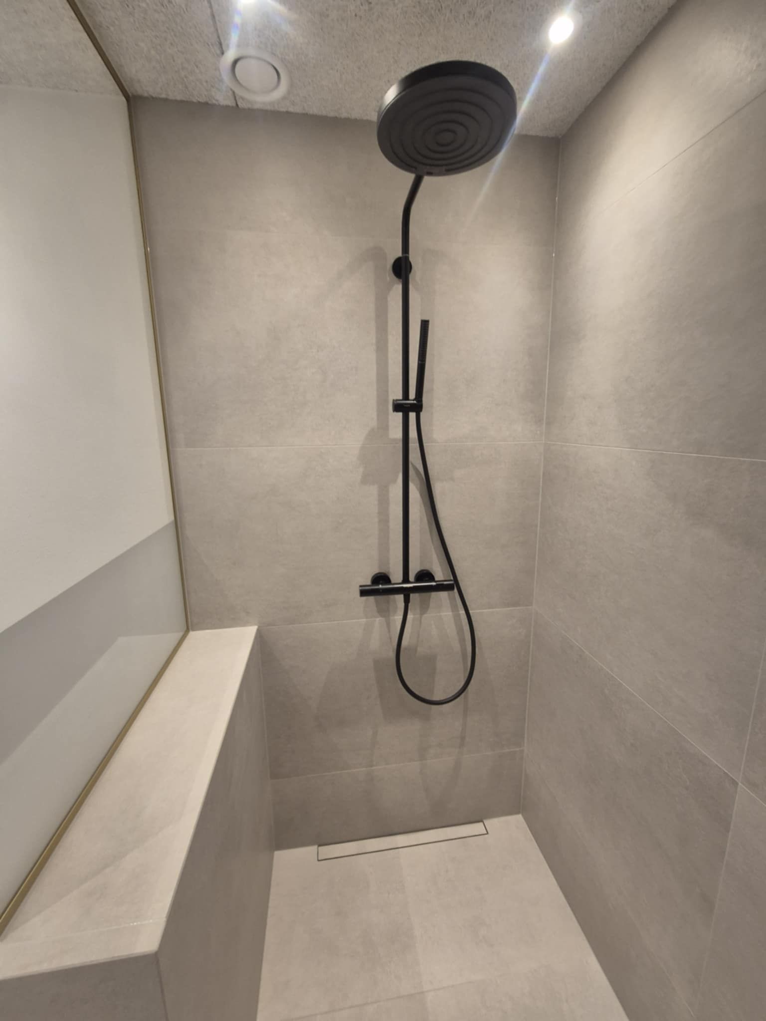 En bruser med sort brusehoved og slange i et badeværelse.