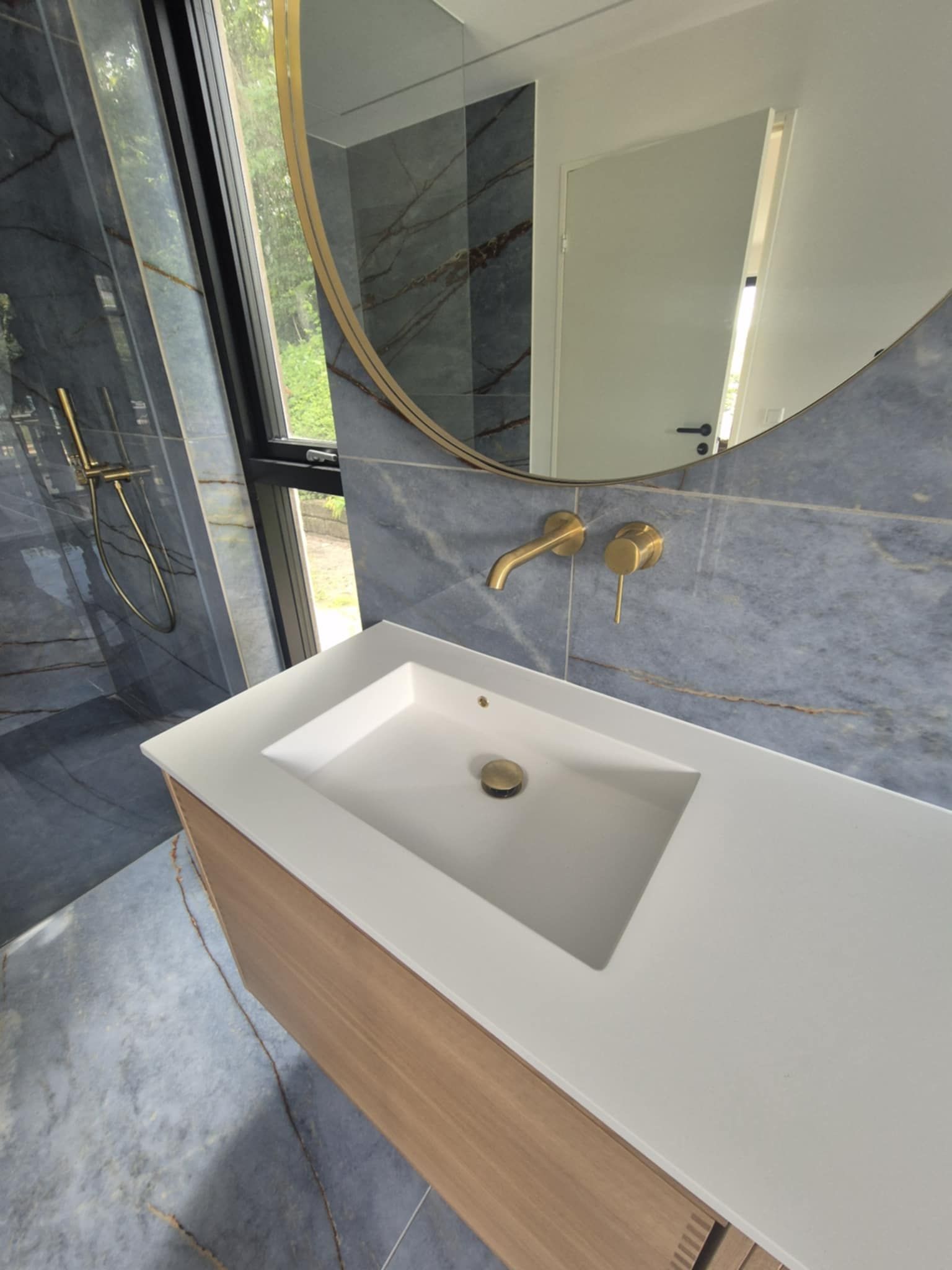 Et badeværelse med håndvask, spejl og bruser.