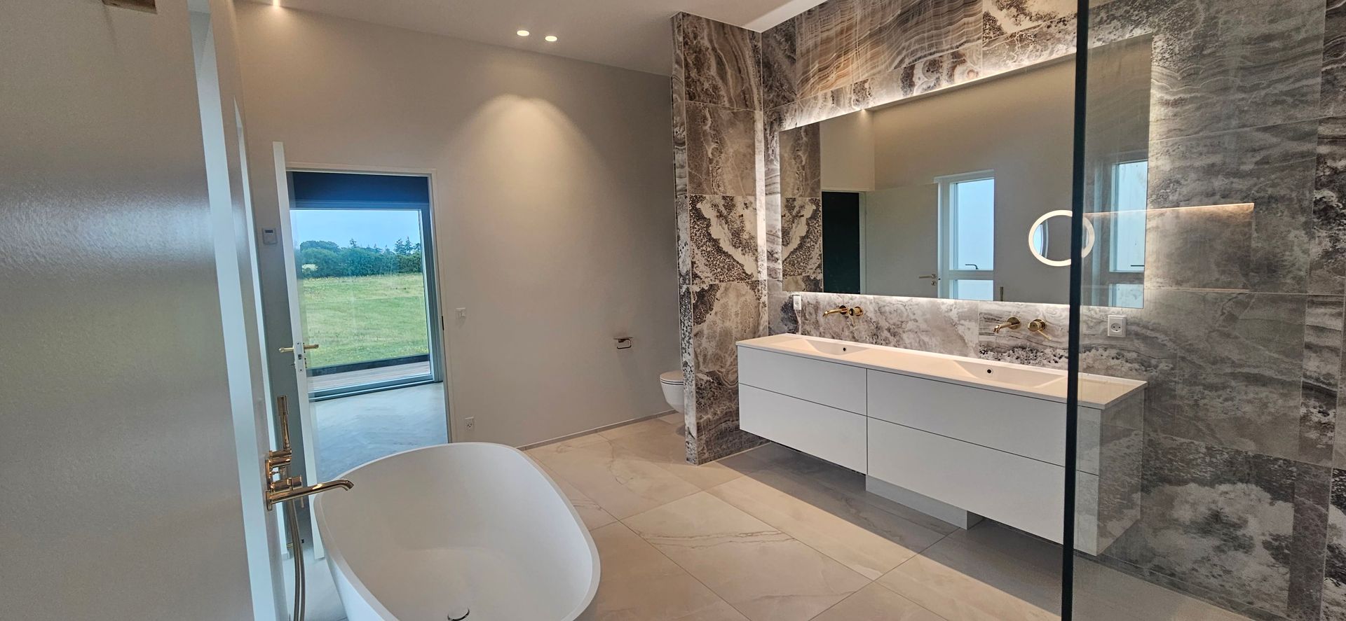 Et badeværelse med badekar, håndvask, spejl og bruseniche.