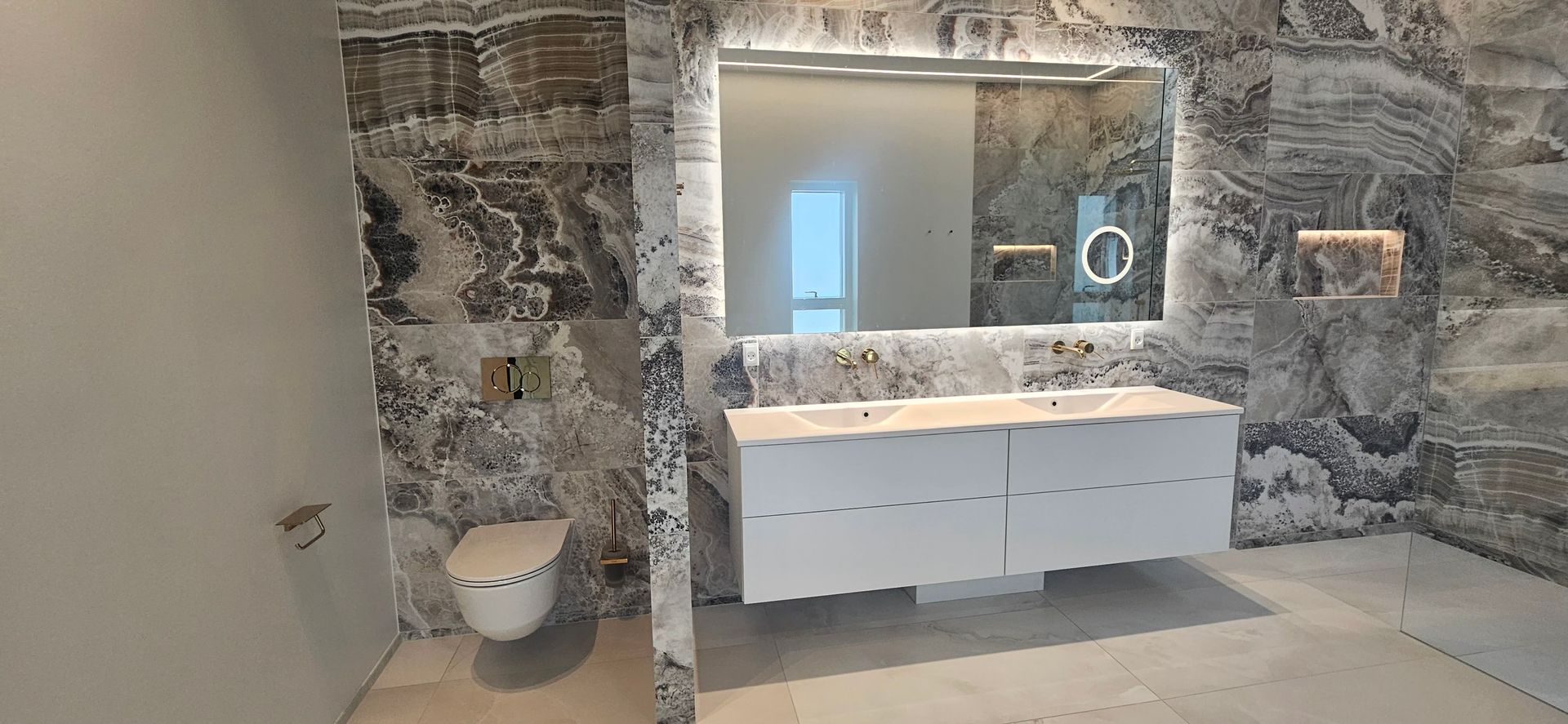 Et badeværelse med to håndvaske, et toilet og et stort spejl.