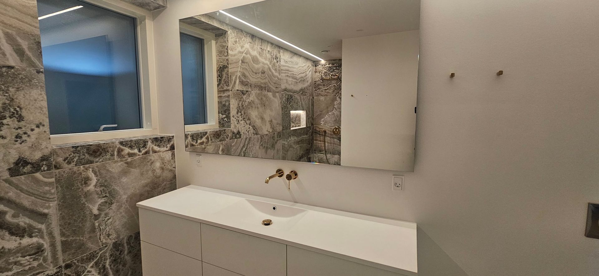 Et badeværelse med vask, spejl og vindue.