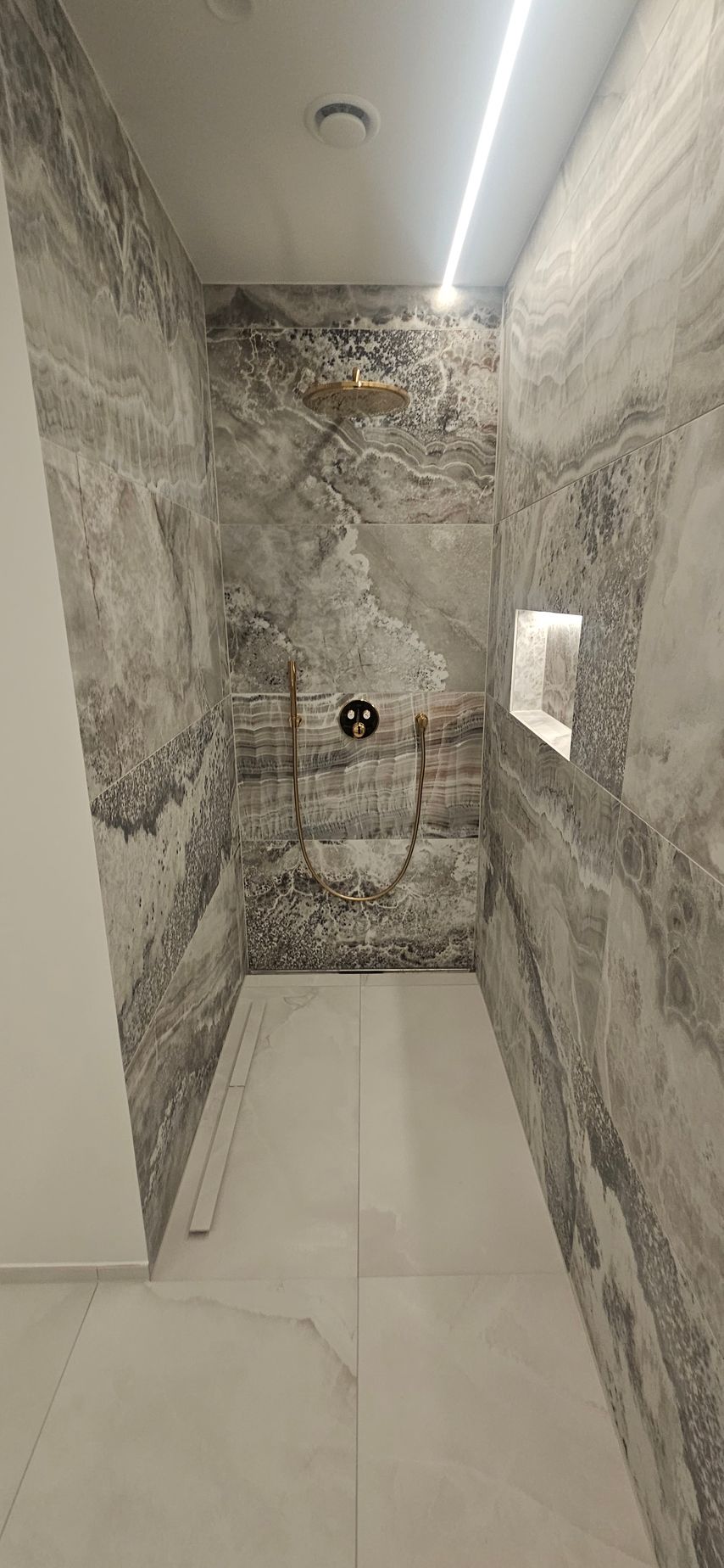Et badeværelse med bruseniche og marmorvæg.