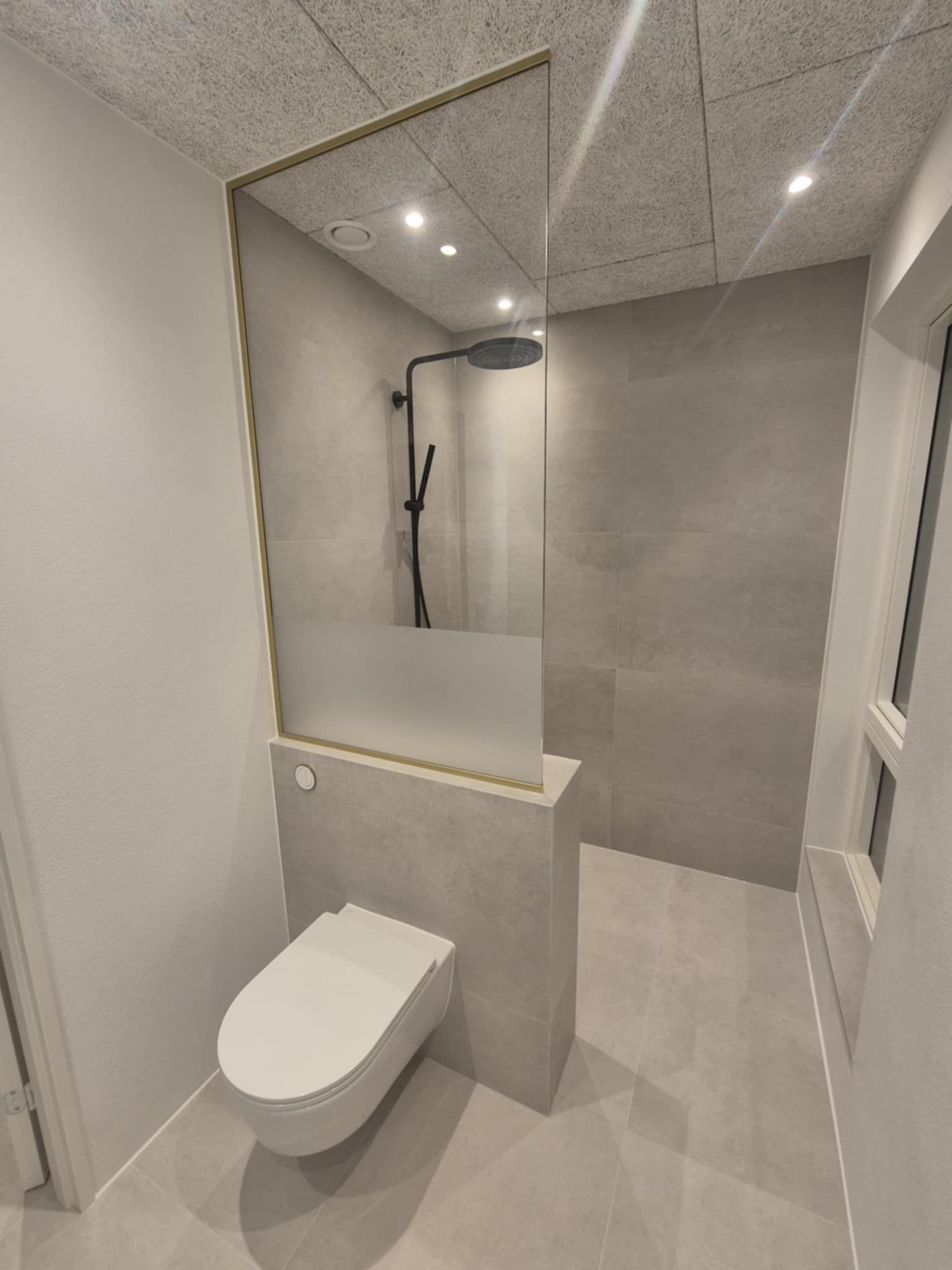 Et badeværelse med toilet, bruser og vindue.