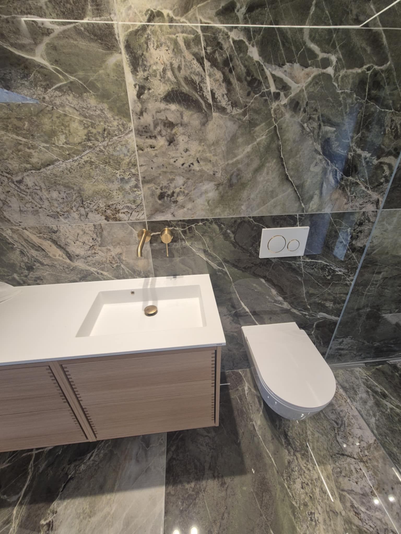 Et badeværelse med håndvask, toilet og marmorfliser.