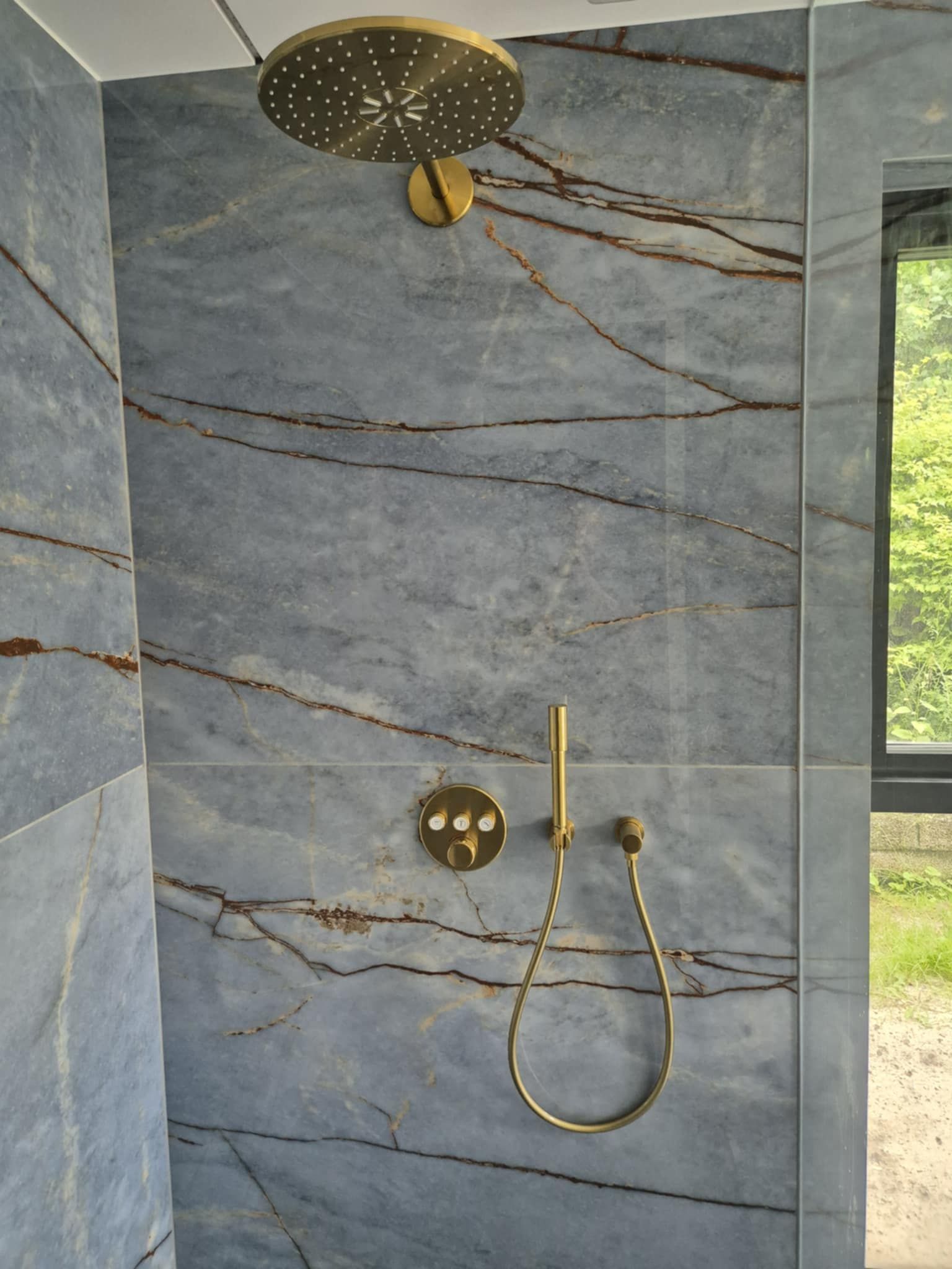 Et brusebad med en marmorvæg og et gyldent brusehoved.