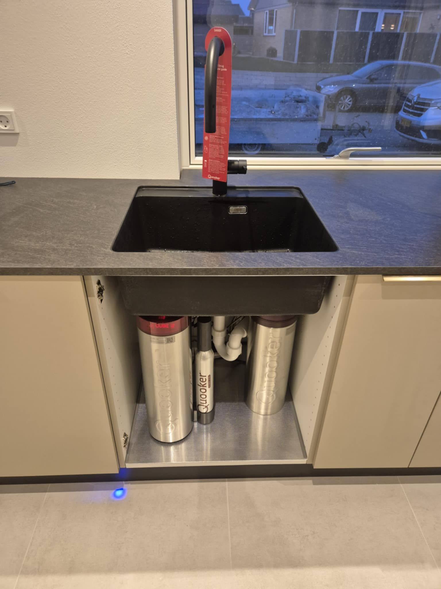 En køkkenvask med en rød vandhane og en skraldespand under.