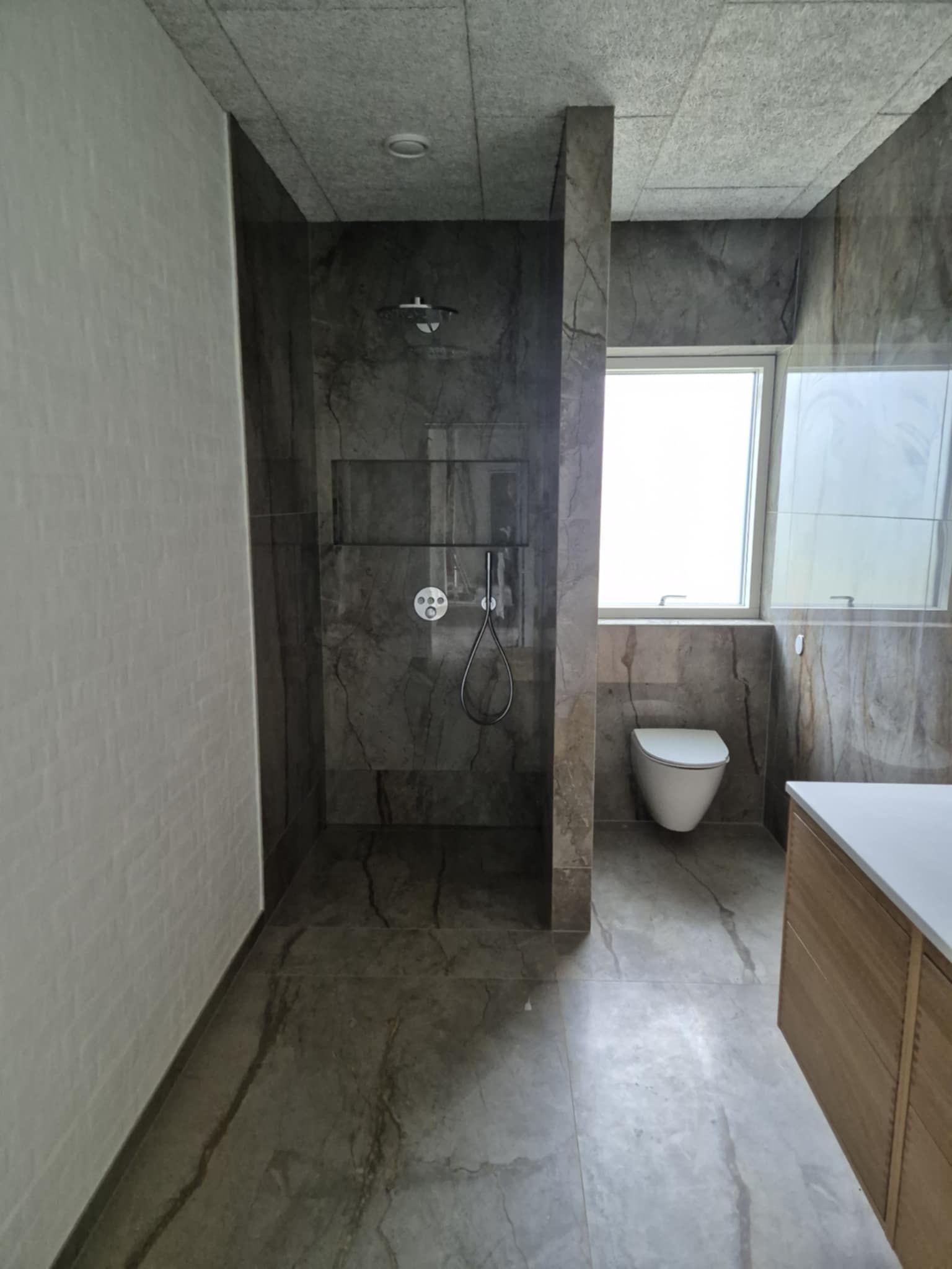 Et badeværelse med toilet, bruser, håndvask og vindue.