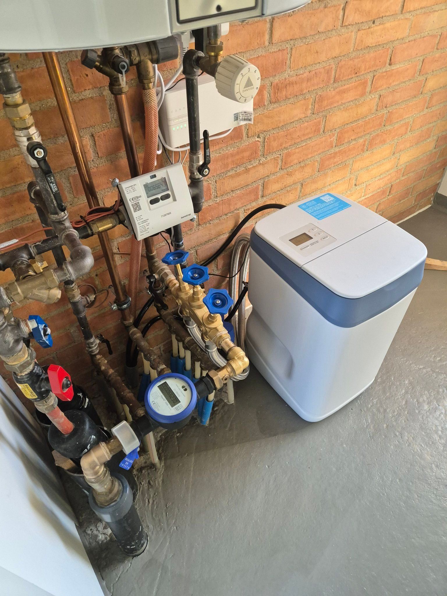 En blødgører sidder på gulvet ved siden af ​​en murstensvæg.