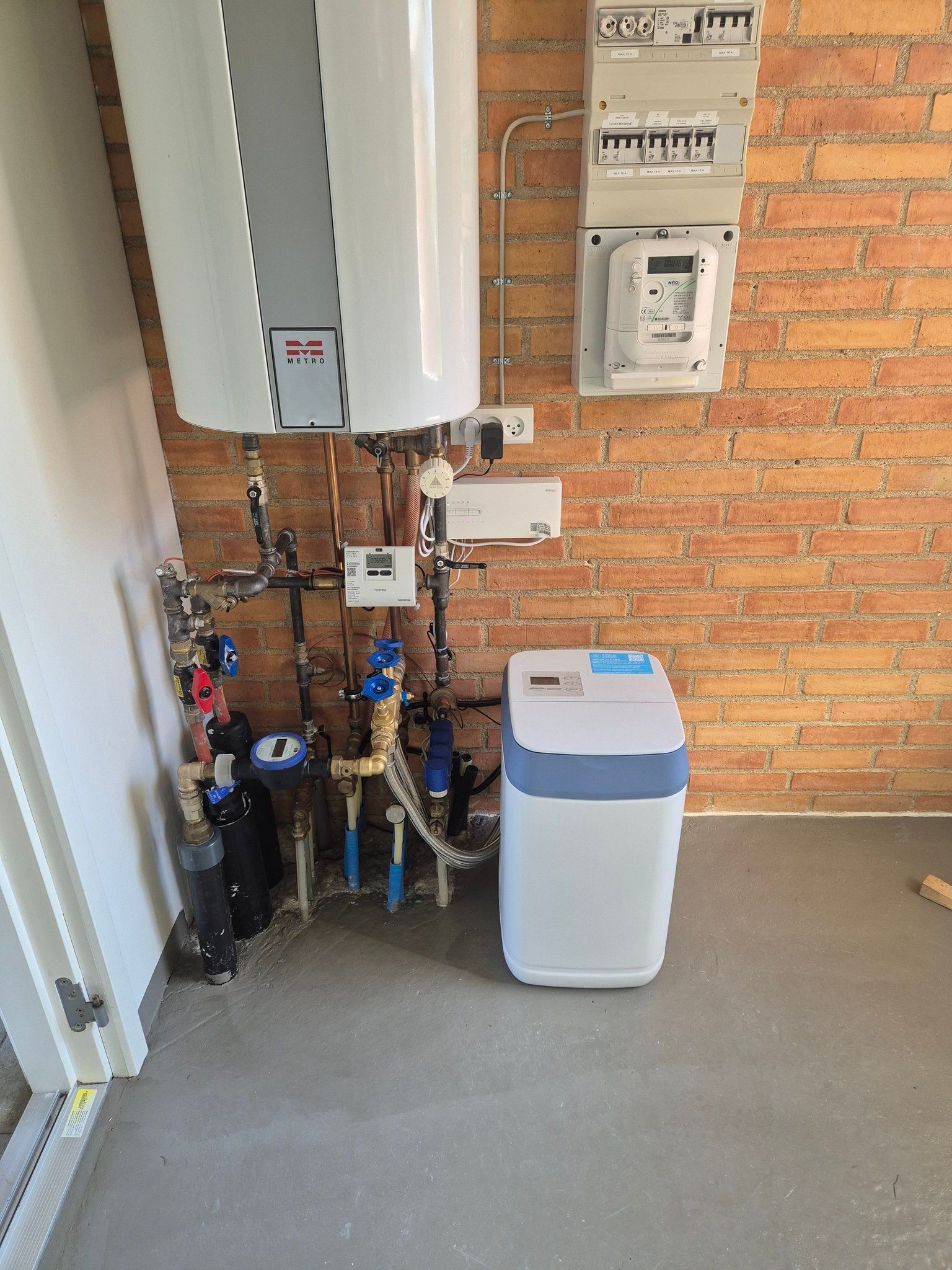 En vandvarmer sidder ved siden af ​​en blødgører i et rum med en murstensvæg.