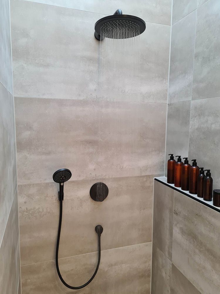 Et badeværelse med brusehoved og flasker på en hylde.