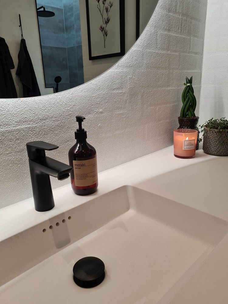 En badeværelsesvask med sort vandhane, sæbedispenser og stearinlys.