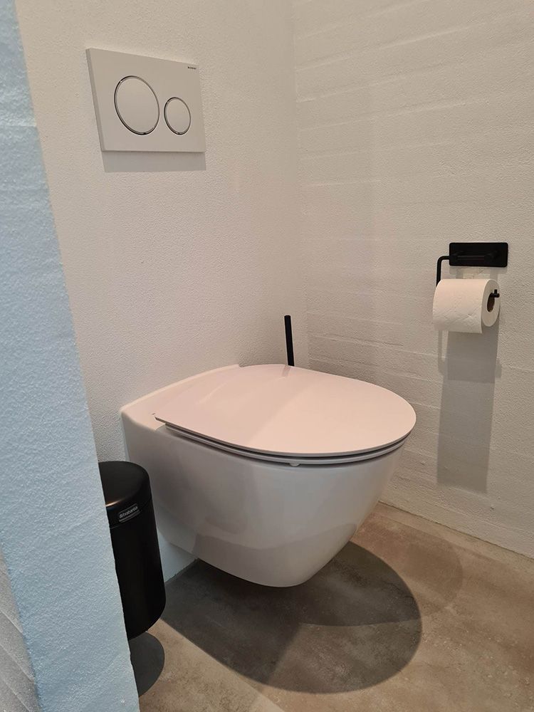 Et hvidt toilet sidder på et badeværelse ved siden af ​​en skraldespand.