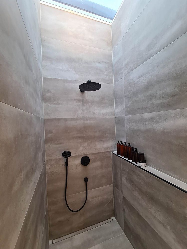 Et badeværelse med bruser og en hylde med flasker på.