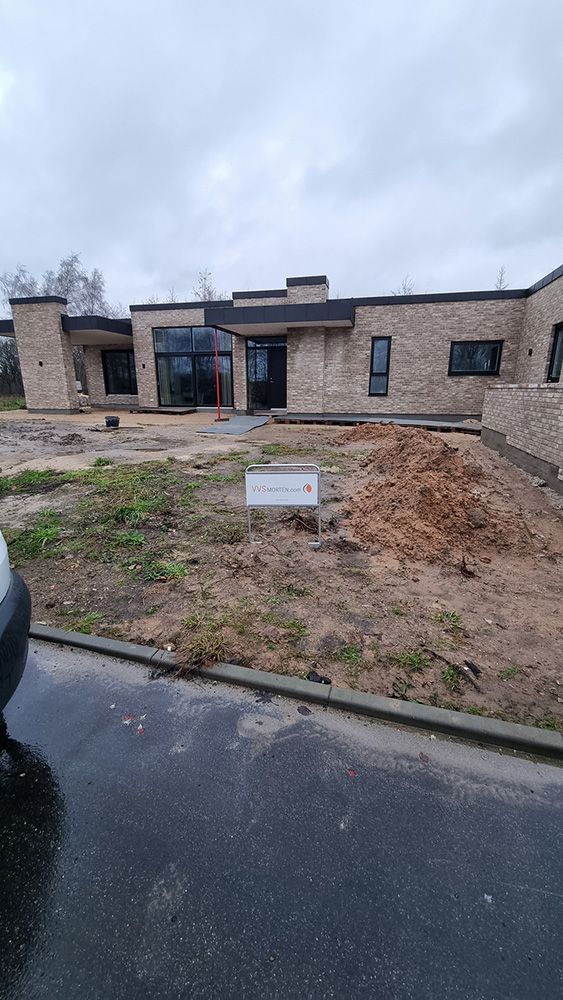 En bil er parkeret foran et stort hus under opførelse.