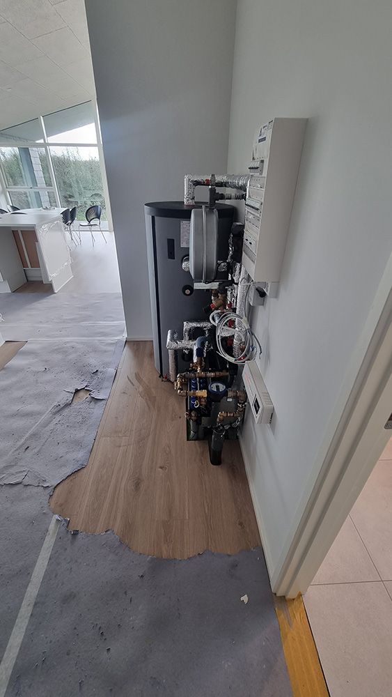 Et sort køleskab står på et trægulv i et rum ved siden af ​​en dør.