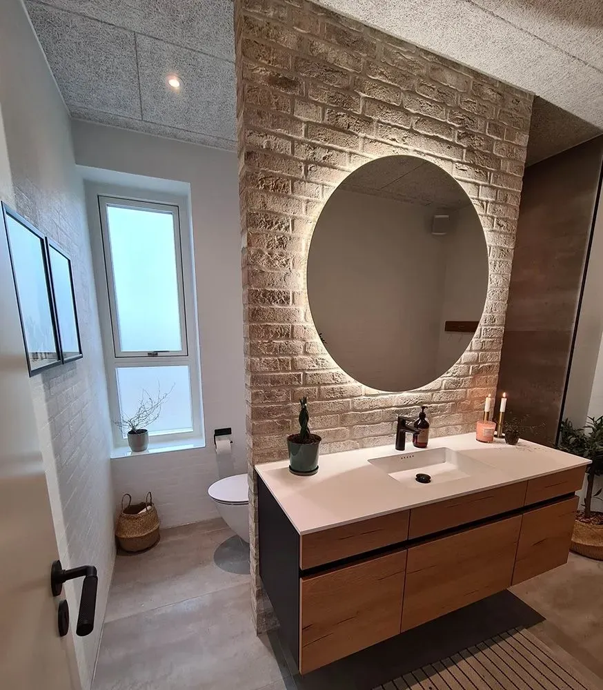 Et badeværelse med håndvask, toilet, spejl og murstensvæg.