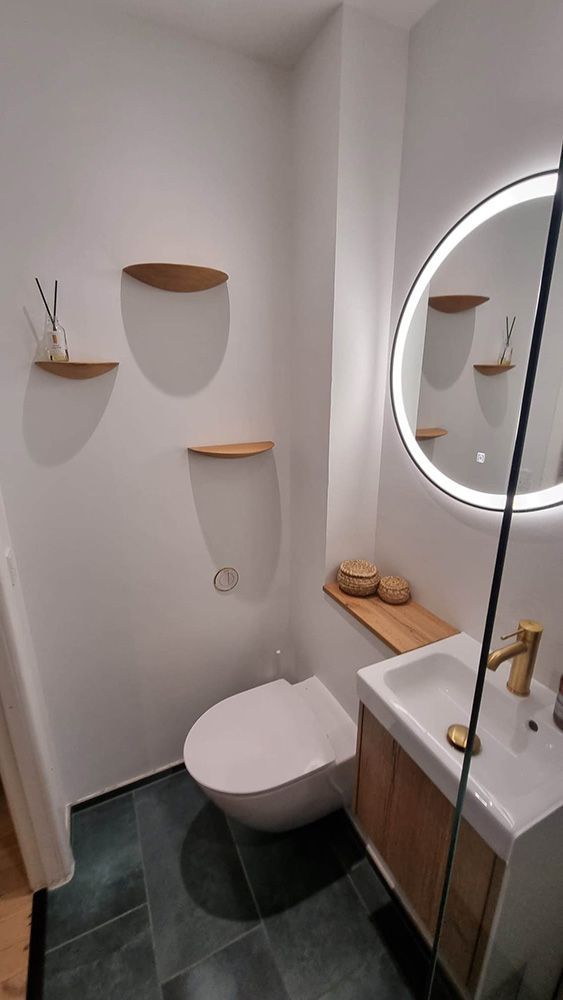Et badeværelse med toilet, håndvask, spejl og hylder.