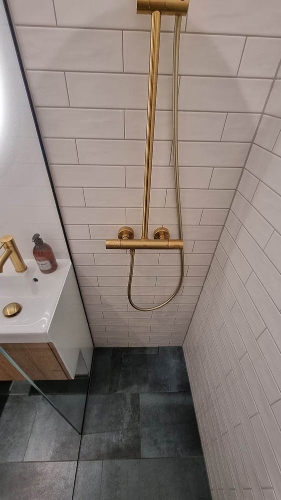 Et badeværelse med håndvask og bruser med guldbrusehoved.