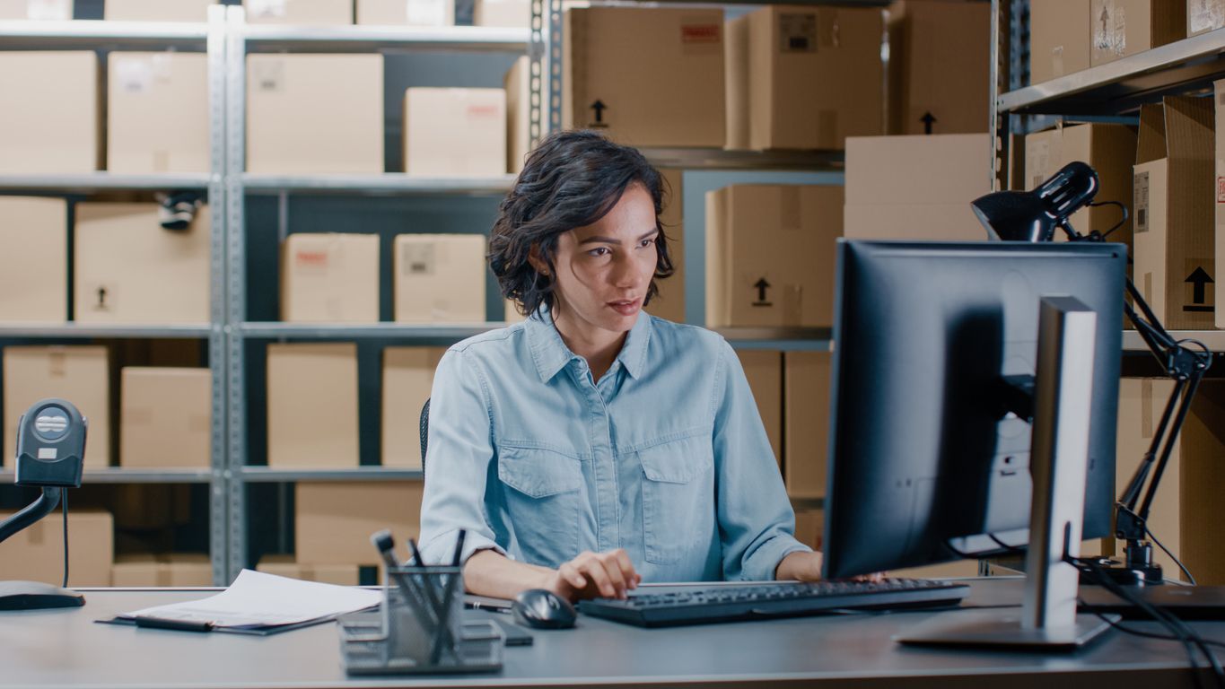 a woman is sitting at a desk in front of a computer in a warehouse .