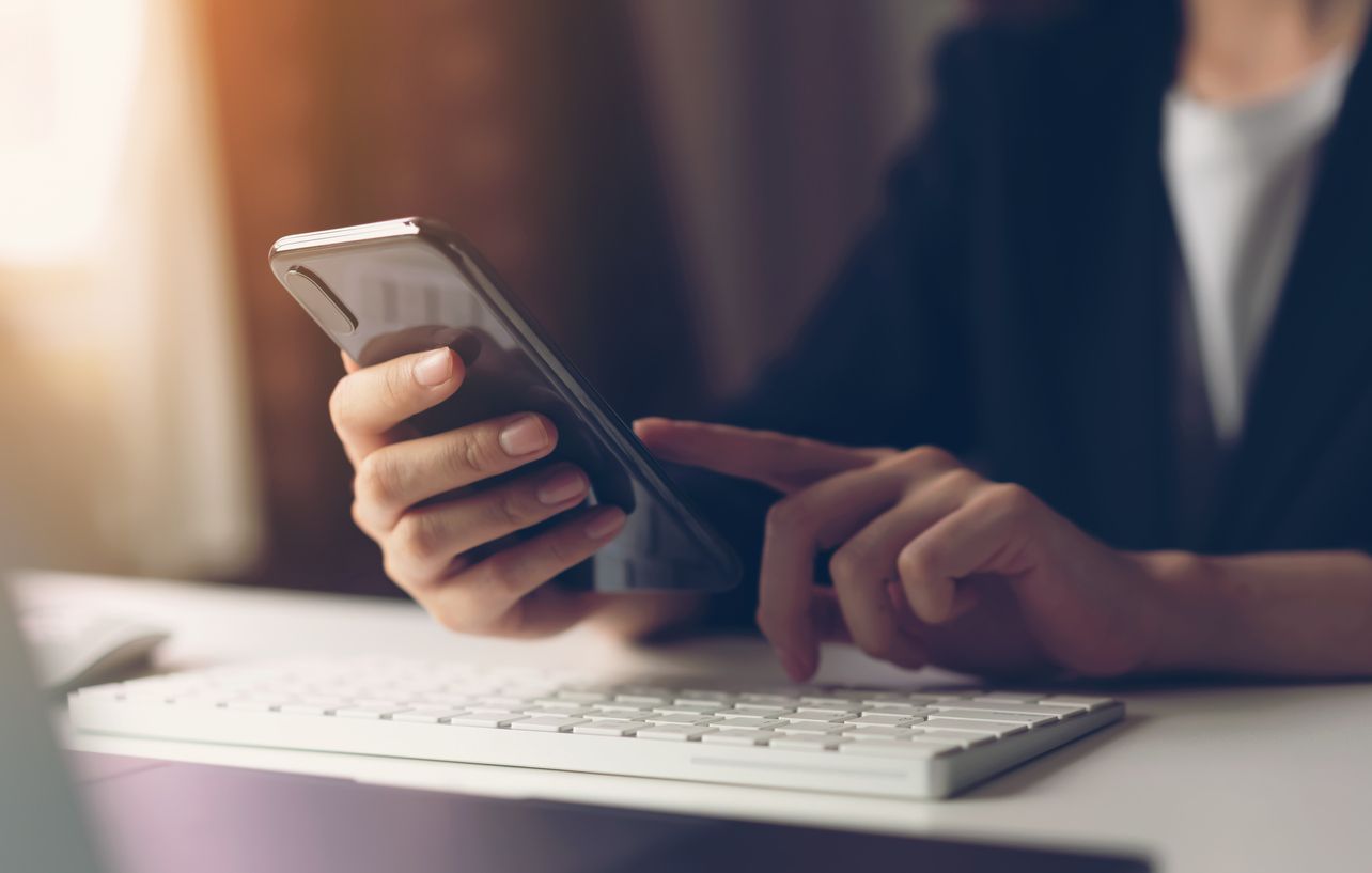 a woman is sitting at a desk using a cell phone .
