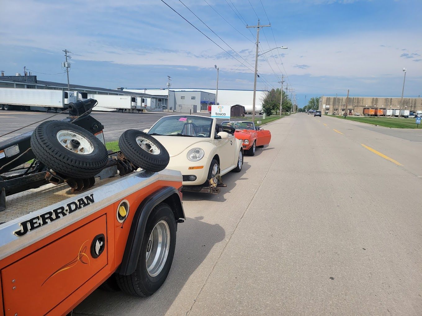 Two cars are being towed by a jerry dan tow truck