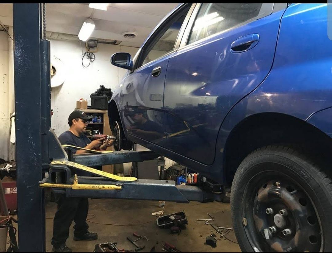 A man is working on a blue car on a lift