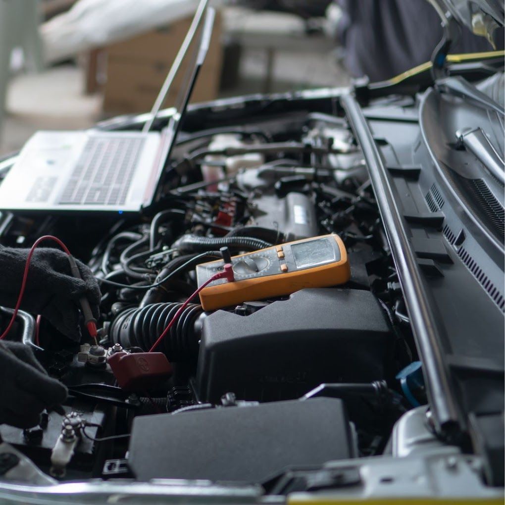 A close up of a car engine with a laptop and a multimeter