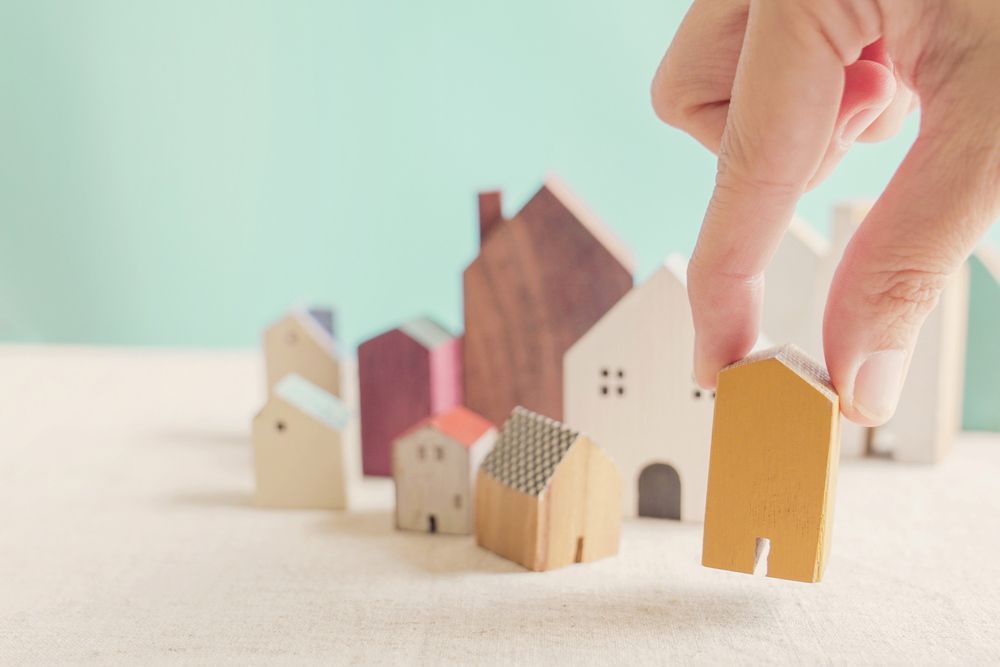 A Person Is Holding a Wooden House in Their Hand in Front of A Group of Wooden Houses — A M Conveyancing Pty Ltd In Tweed Heads, NSW
