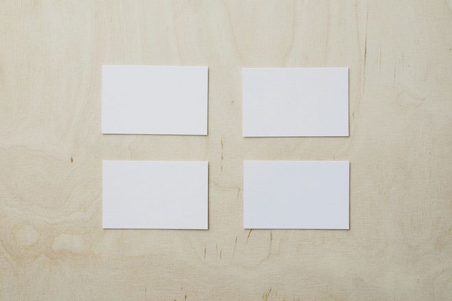 Four blank white business cards on a light wood grain background.