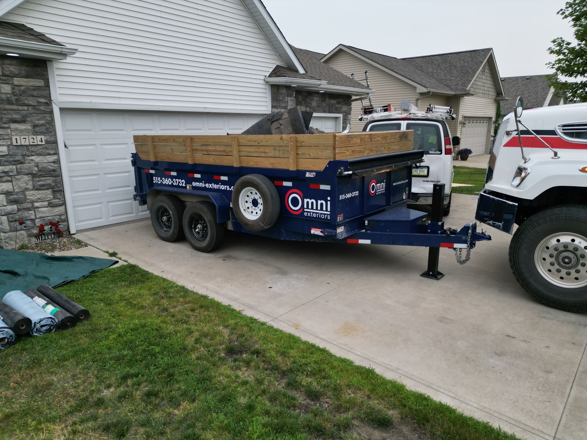 A dumpster is parked in front of a house next to a truck.