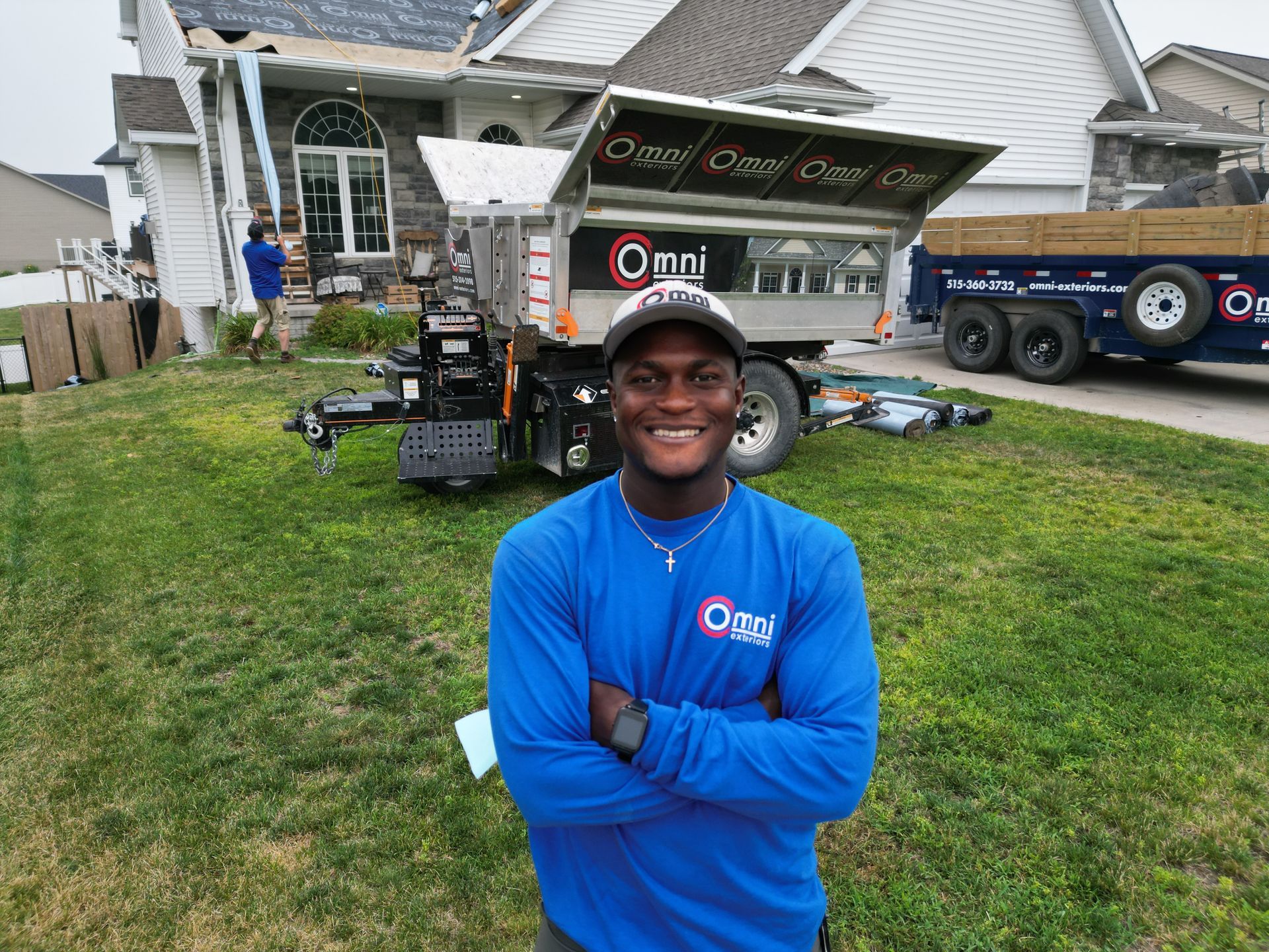 A man in a blue shirt is standing in front of a house with his arms crossed.