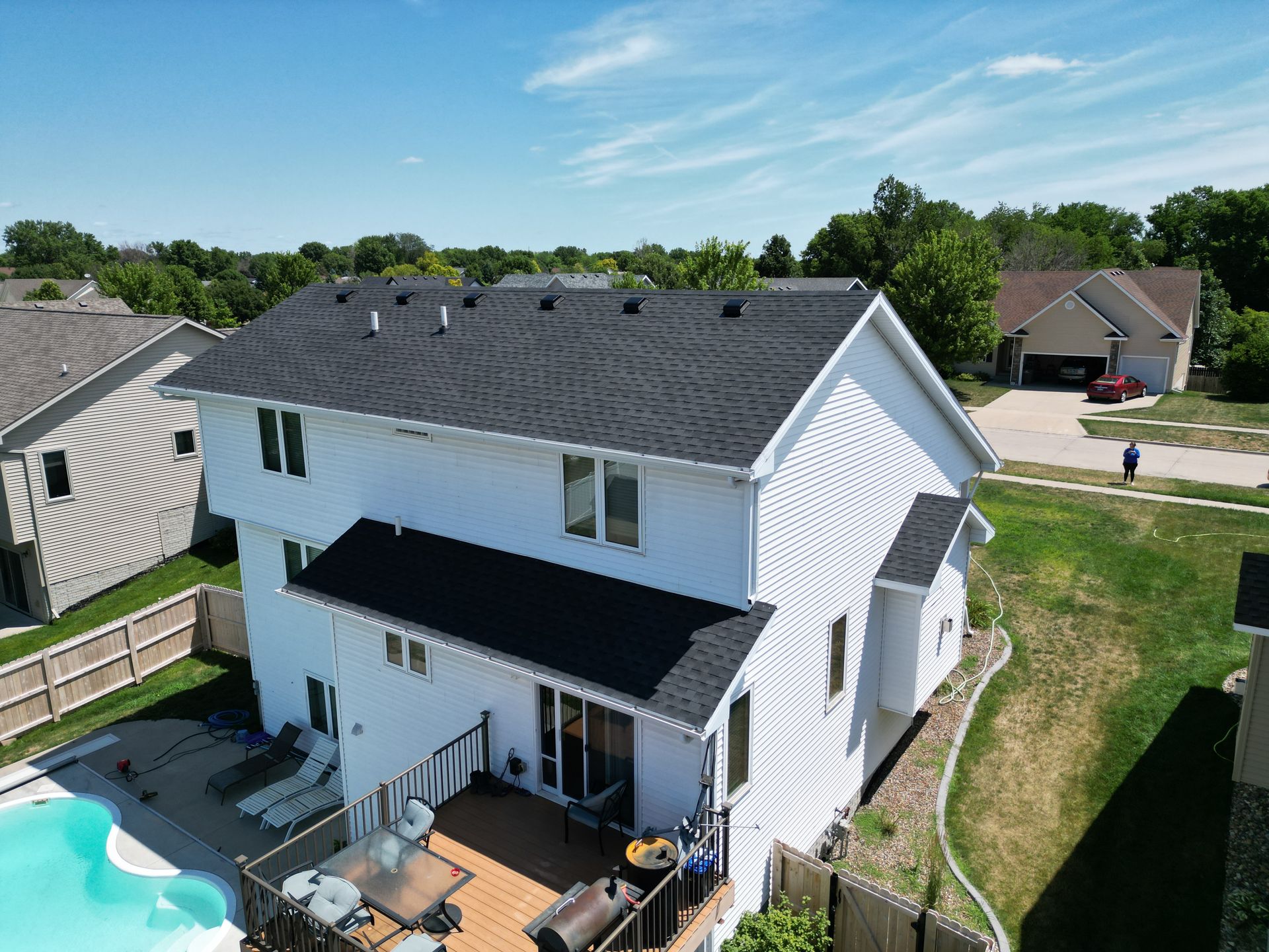 An aerial view of a white house with a black roof and a pool.