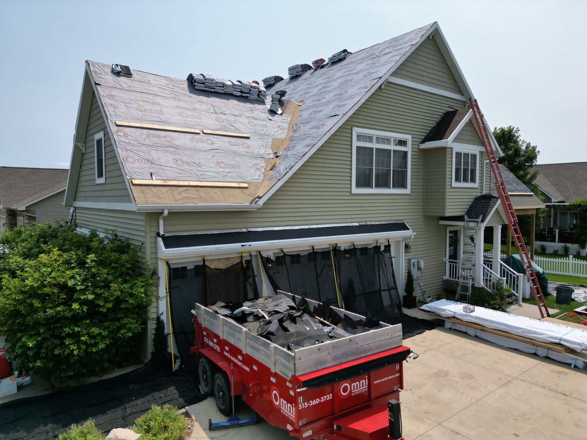 A house with a roof being installed and a dumpster in front of it.